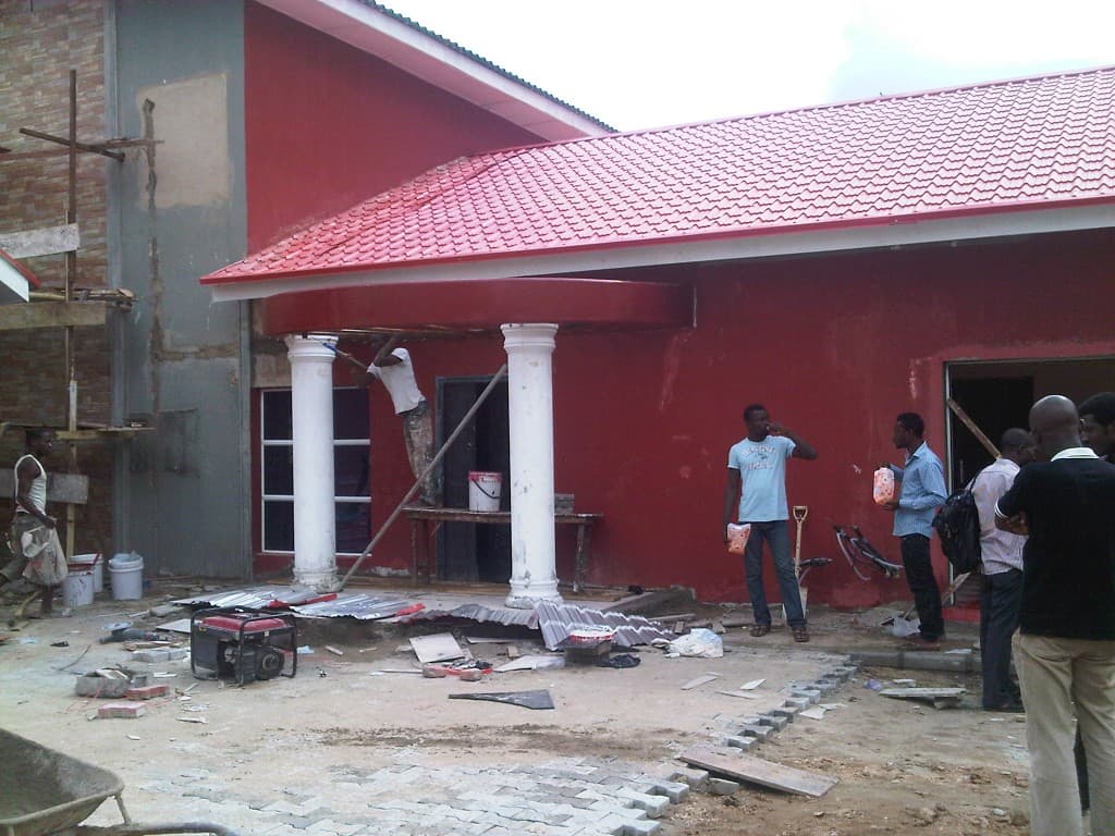 Workers finishing the red entrance facade and white columns at Our Place